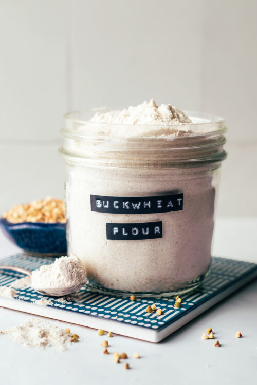 Jar of homemade buckwheat flour next to a bowl of buckwheat groats used to make it
