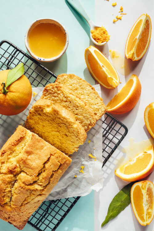 Sliced oranges next to a partially sliced orange almond loaf cake